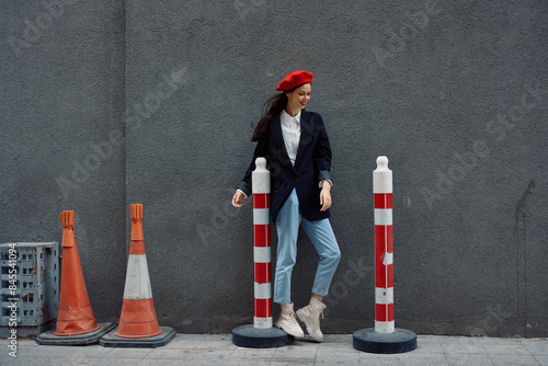 Fashion woman standing leaning against a wall street against a background of the city road works tourist in stylish clothes with red lips and red beret, travel, cinematic color, retro vintage style.