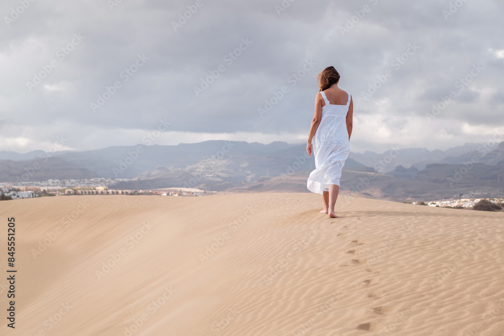 Woman walking among dunes at sunset in a paradise destination. Concept: vacation, enjoy Woman walking among dunes at sunset in a paradise destination. Concept: vacation, enjoy