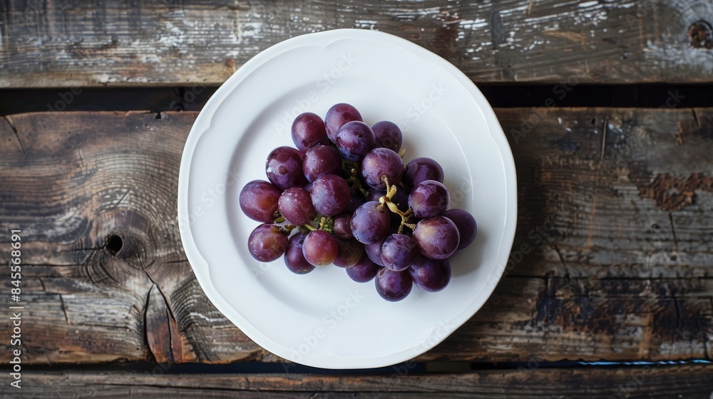 Close-up shot of purple grapes on a clean white plate, with a rustic wooden table underneath. Close-up shot of purple grapes on a clean white plate, with a rustic wooden table underneath.