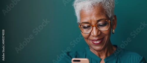 A Mature Woman With Grey Hair Uses a Smartphone Against a Teal Background
