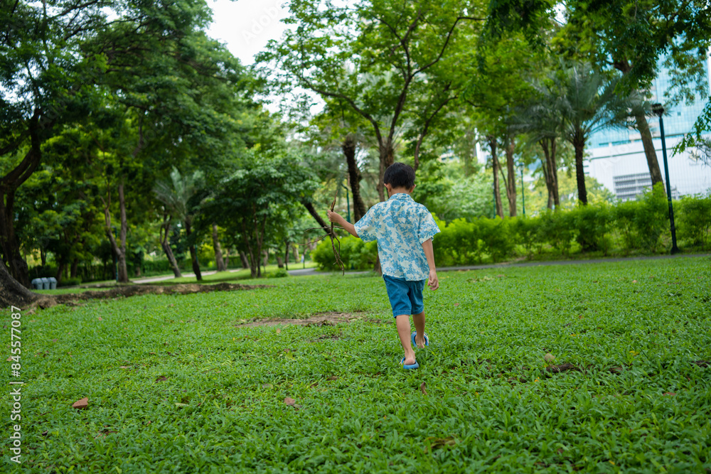 Happy asian preschool boy walking in green tropical tree forest in city park