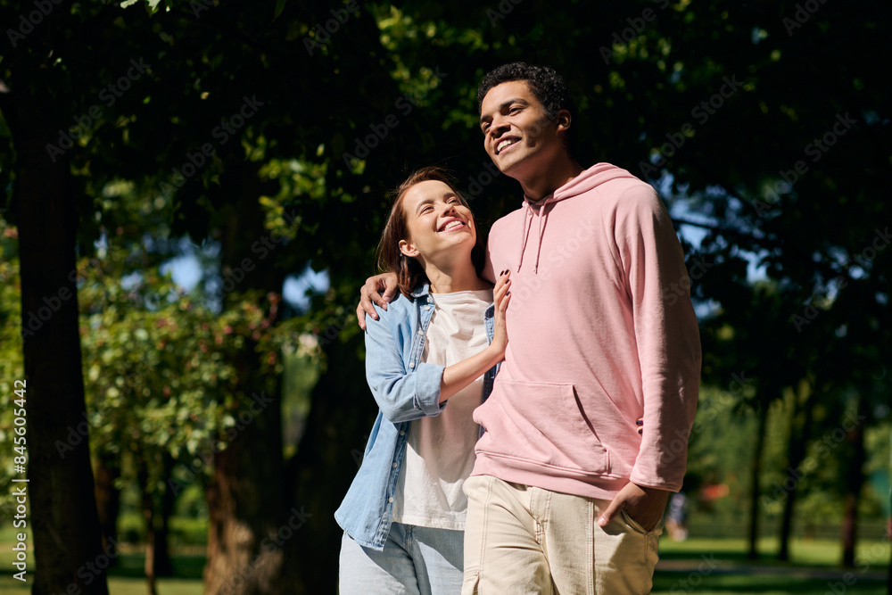 A diverse couple, dressed in vibrant attires, stands together in a park, radiating love and togetherness. A diverse couple, dressed in vibrant attires, stands together in a park, radiating love and togetherness.