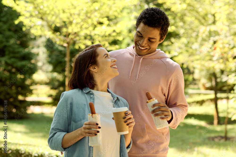 A stylish and diverse couple enjoying each others company while holding coffee cups in a vibrant park setting. A stylish and diverse couple enjoying each others company while holding coffee cups in a vibrant park setting.