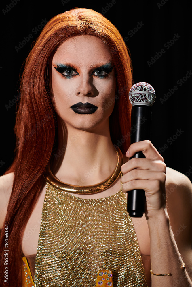 Fototapeta premium A drag queen in a gold chainmail top holds a microphone, ready to perform.