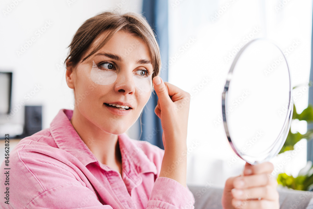 Cute, beautiful, middle aged woman with patches under her eyes on her face looking in mirror Cute, beautiful, middle aged woman with patches under her eyes on her face looking in mirror