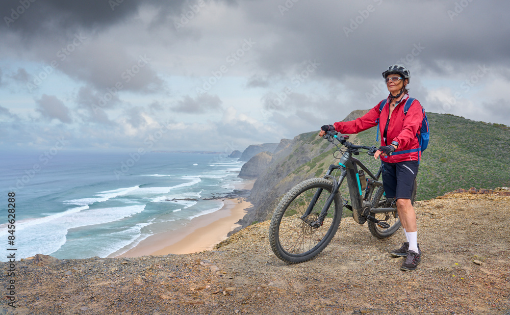 Obraz premium happy active senior woman cycling on the the rocky cliffs of the Vicentina coast of Algarve, Portugal near Sagres and Vila do Bispo 