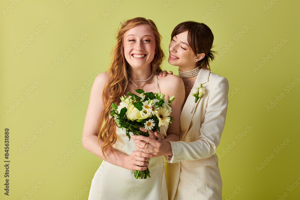 Two brides, dressed in white, share a joyous moment on their wedding day. The bride on the left holds a bouquet of white flowers, while the bride on the right has her arm around her partner. Two brides, dressed in white, share a joyous moment on their wedding day. The bride on the left holds a bouquet of white flowers, while the bride on the right has her arm around her partner.