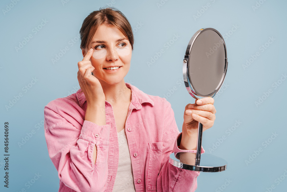 Smiling attractive woman with face patches looking in mirror, morning routine Smiling attractive woman with face patches looking in mirror, morning routine