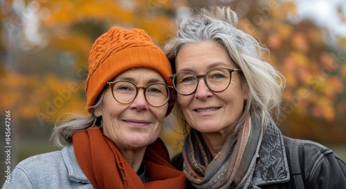 Two Smiling Women In Orange Hats Stand Close Together During Fall