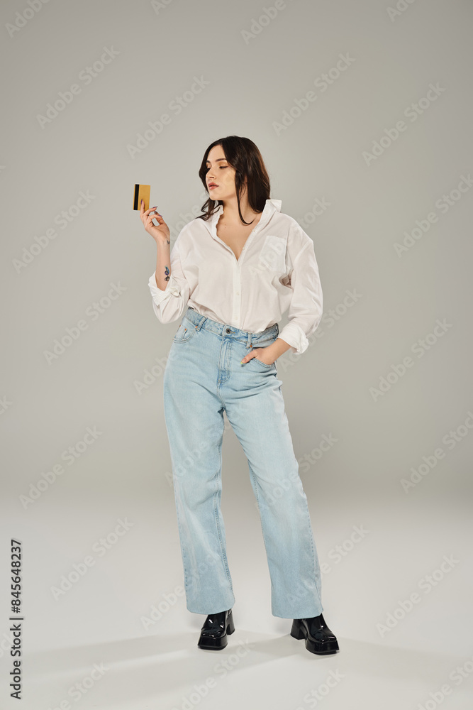 Stylish plus-size woman in white shirt delicately holds credit card against a sleek gray backdrop. Stylish plus-size woman in white shirt delicately holds credit card against a sleek gray backdrop.