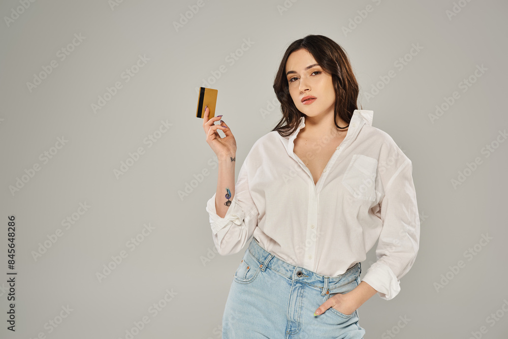 Beautiful plus-size woman in a white shirt confidently holding a gold card against a gray backdrop. Beautiful plus-size woman in a white shirt confidently holding a gold card against a gray backdrop.