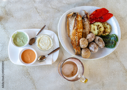 Papas arrugadas, grilled fish, grilled vegetables, red mojo, green mojo, beer mug. Traditional Canarian food