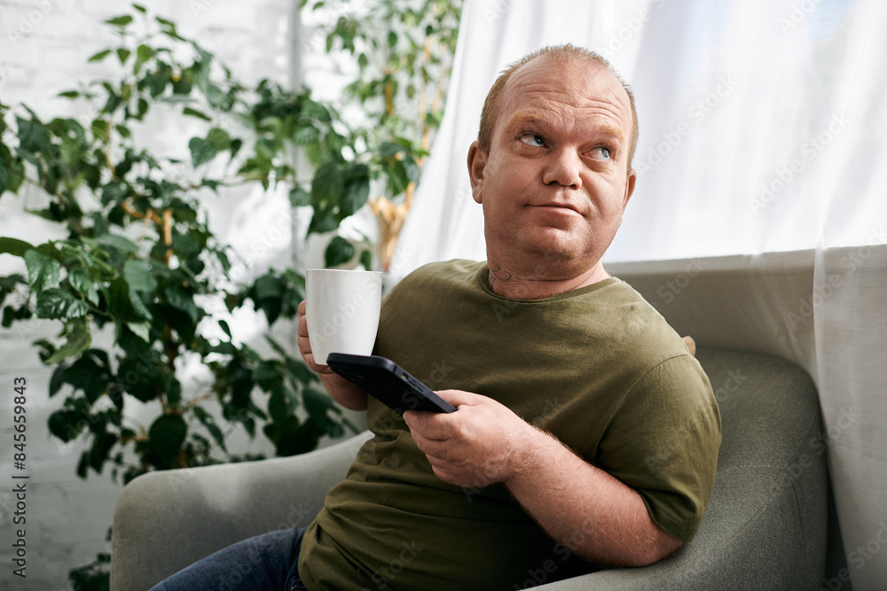 A man with inclusivity sits in a chair, holding a coffee mug and looking up thoughtfully. A man with inclusivity sits in a chair, holding a coffee mug and looking up thoughtfully.