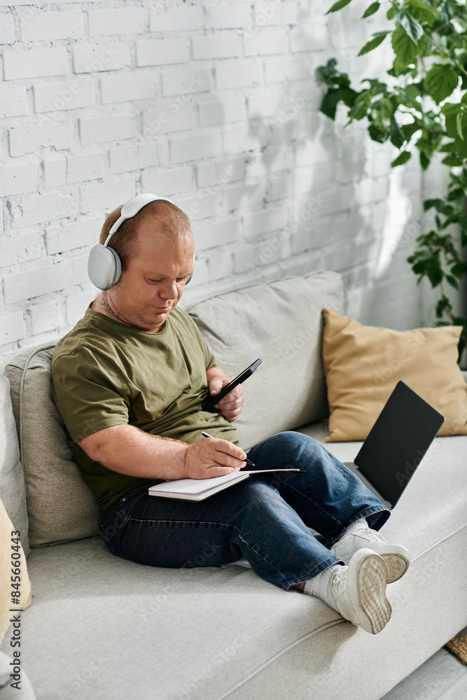 A man with inclusivity wearing headphones sits comfortably on a couch, taking notes in a notebook. A man with inclusivity wearing headphones sits comfortably on a couch, taking notes in a notebook.