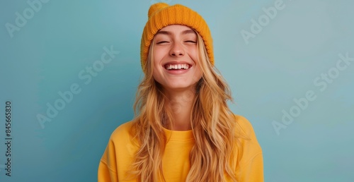 Smiling Young Woman Wearing a Yellow Hoodie and Beanie Against a Blue Background
