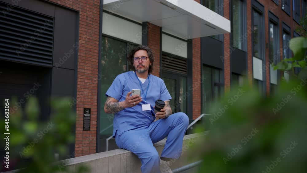 Healthcare worker taking a break, scrolling a phone and drinking coffee outdoors, in front of the hospital. Healthcare worker taking a break, scrolling a phone and drinking coffee outdoors, in front of the hospital.