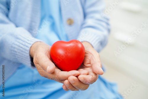 Asian elderly woman holding red heart in her hand in hospital.