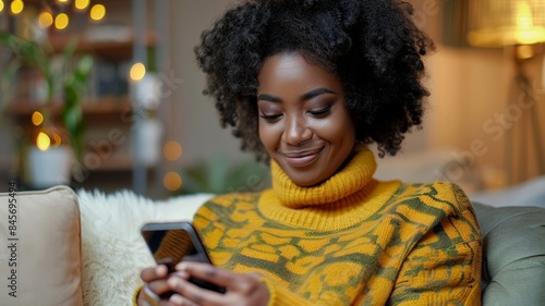 Smiling Black Woman Using Her Smartphone While Relaxing on a Couch at Home