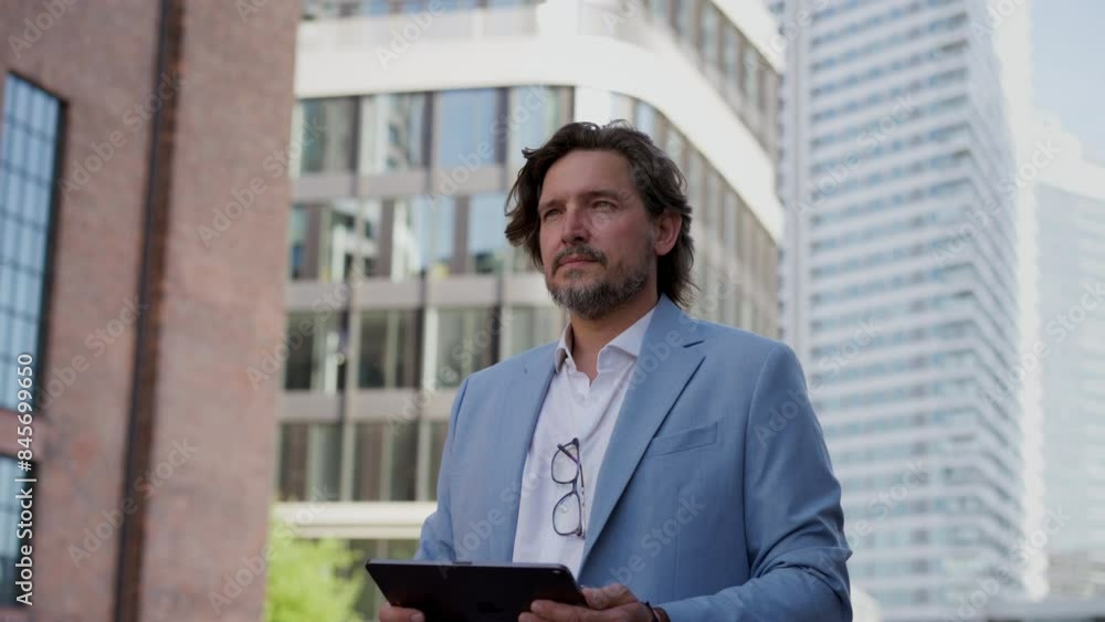 Video of mature businessman with tablet, walking on city street, in front of office building. Handsome man with glasses in suit. Video of mature businessman with tablet, walking on city street, in front of office building. Handsome man with glasses in suit.