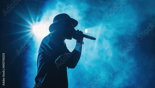 Silhouette of rap singer performing on stage. Bright blue background with hip hop artist performing on concert in night club 