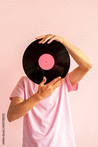 Portrait of man in pink shirt holding vinyl record near his face on pink background.