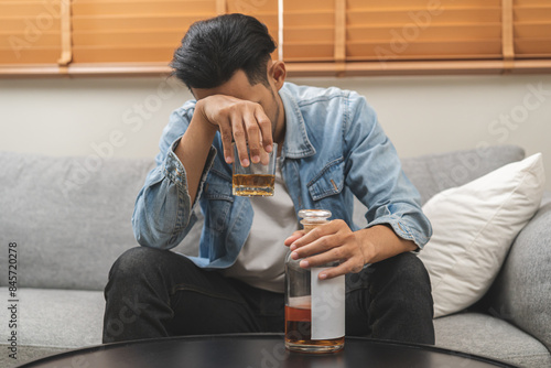 Health care alcoholism drunk, fatigue asian young man drinking beverage on table, alone depressed male drink booze on sofa at home. Treatment of alcohol addiction, suffer abuse problem alcoholism. photo