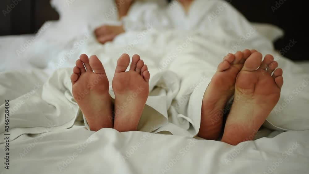 Man scratches his leg with other leg. Bare feet covered with blanket close up. Young couple in love lying in bed in white bedding. Male and female legs bare. Morning newlyweds wedding barefoot Man scratches his leg with other leg. Bare feet covered with blanket close up. Young couple in love lying in bed in white bedding. Male and female legs bare. Morning newlyweds wedding barefoot