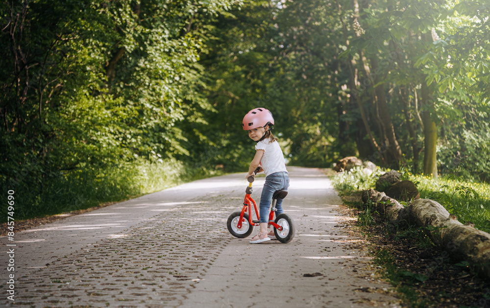 a little girl in a bicycle helmet rides a balance bike in the park