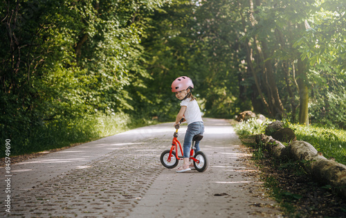 Obraz na płótnie a little girl in a bicycle helmet rides a balance bike in the park w salonie
