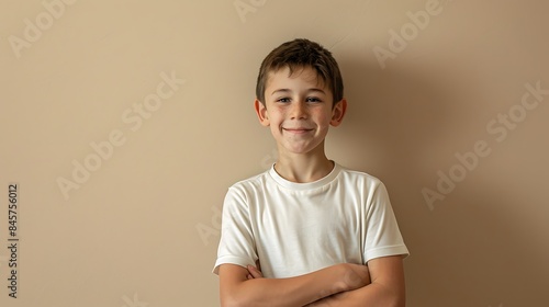 A high-quality, realistic photo of a boy in a simple t-shirt, standing with a smile and arms crossed. The background is beige, enhancing the portraita??s clarity and detail. photo