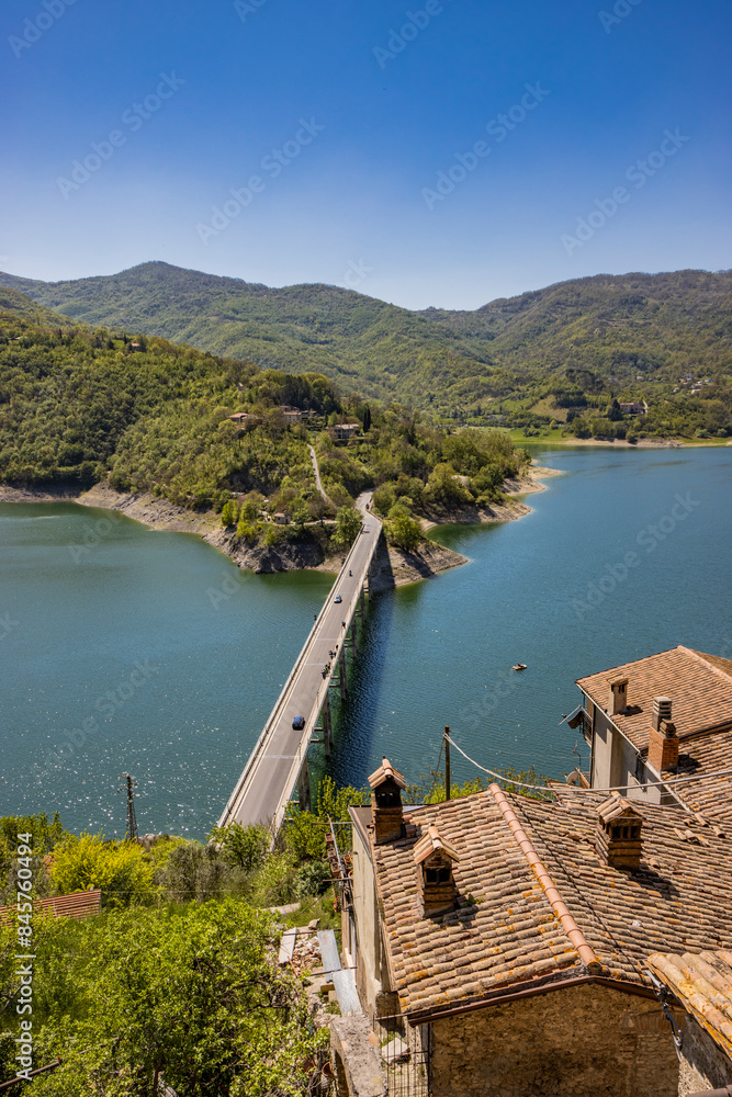 Obraz premium A view of Lake Turano, from the village of Castel di Tora, Rieti, Lazio, Italy. The bridge crossing the lake, surrounded by green mountains. Blue sky in summer.