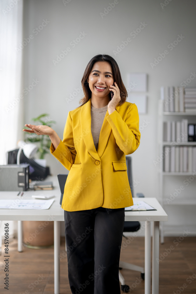 A woman in a yellow jacket is talking on her cell phone in a room with a desk A woman in a yellow jacket is talking on her cell phone in a room with a desk