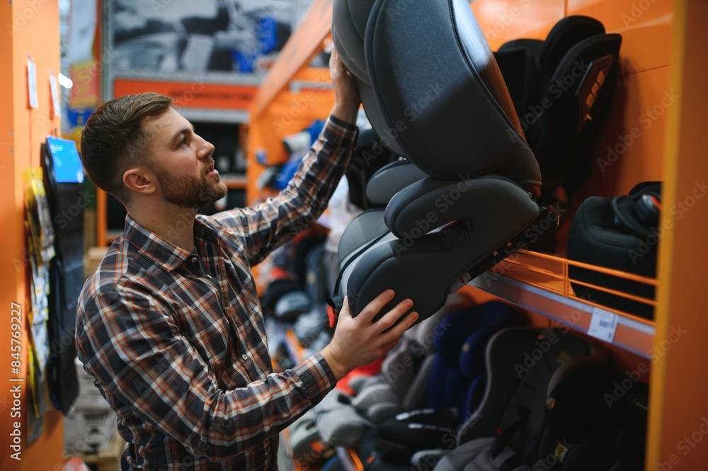 Young father with choosing car seat in store of children's goods Young father with choosing car seat in store of children's goods