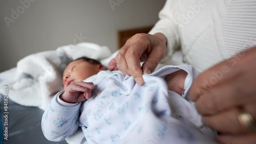 Newborn baby being carefully dressed in a soft white onesie by gentle hands. baby lies peacefully on a soft blanket, showcasing tender caregiving moments and early stages of life photo