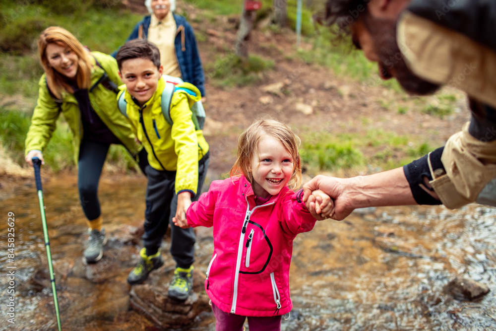 Multi-generational family crossing a stream during a forest hike Multi-generational family crossing a stream during a forest hike