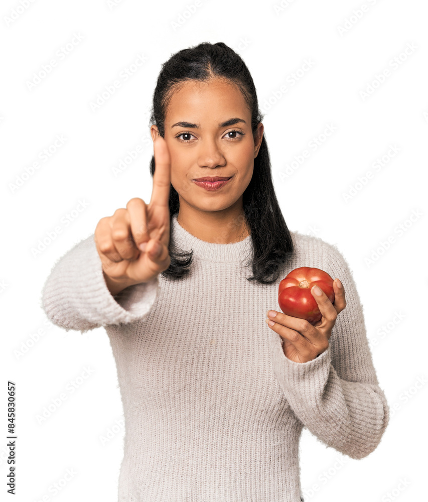 Young Filipina holding a tomato showing number one with finger. Young Filipina holding a tomato showing number one with finger.