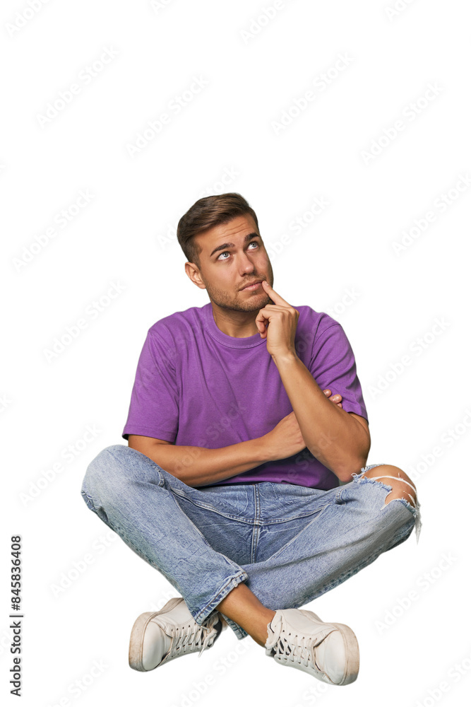 Casual man sitting on floor looking sideways with doubtful and skeptical expression. Casual man sitting on floor looking sideways with doubtful and skeptical expression.
