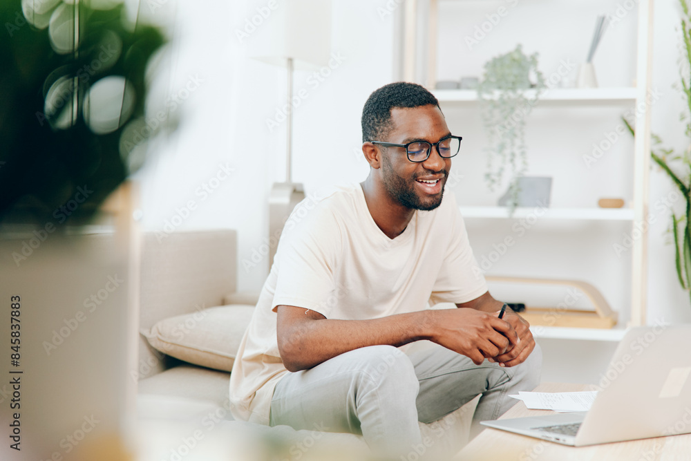 Smiling African American Freelancer Working on Laptop in Modern Home Office A young African American guy is sitting on a comfortable sofa in his modern living room, working on his laptop With a Smiling African American Freelancer Working on Laptop in Modern Home Office A young African American guy is sitting on a comfortable sofa in his modern living room, working on his laptop With a