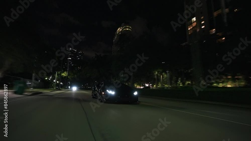 Rolling shot of  black supercar driving at night on the streets in Miami Florida city with skyline city lights view