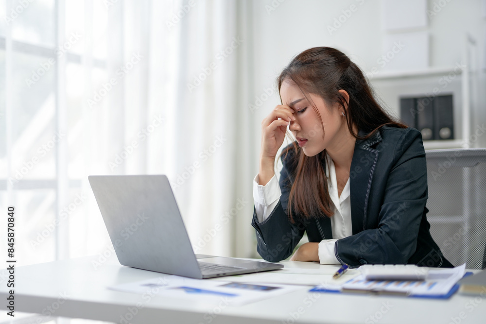 Businesswoman feeling stress and headache while working on a laptop at the office desk. Overworked and fatigue concept. Businesswoman feeling stress and headache while working on a laptop at the office desk. Overworked and fatigue concept.