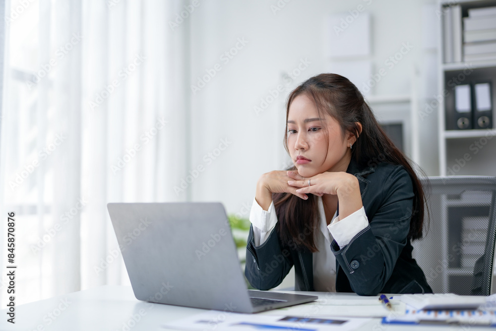 Businesswoman in an office working on a laptop with a thoughtful expression, dealing with workplace challenges and tasks in a professional setting. Businesswoman in an office working on a laptop with a thoughtful expression, dealing with workplace challenges and tasks in a professional setting.