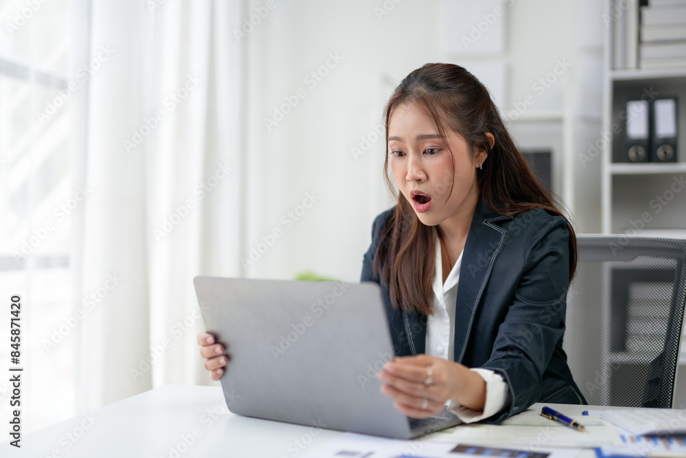 Shocked businesswoman in office suit staring at a laptop, reacting to surprising news or information, sitting at her desk in a modern office. Shocked businesswoman in office suit staring at a laptop, reacting to surprising news or information, sitting at her desk in a modern office.