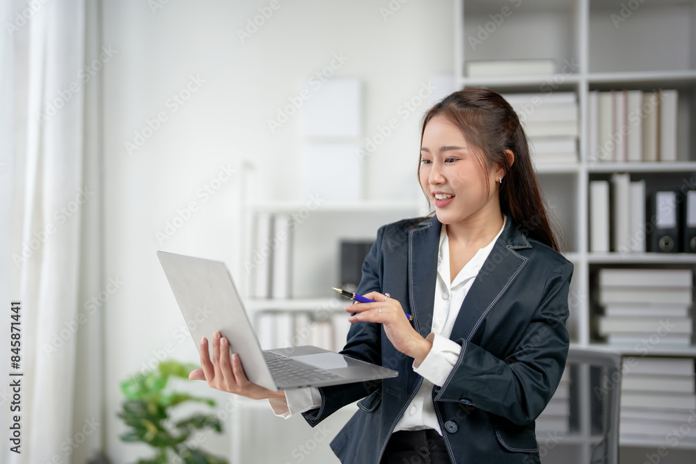 Smiling businesswoman holding a laptop and pen in office, confidently working. Professional attire, modern workspace in the background. Smiling businesswoman holding a laptop and pen in office, confidently working. Professional attire, modern workspace in the background.