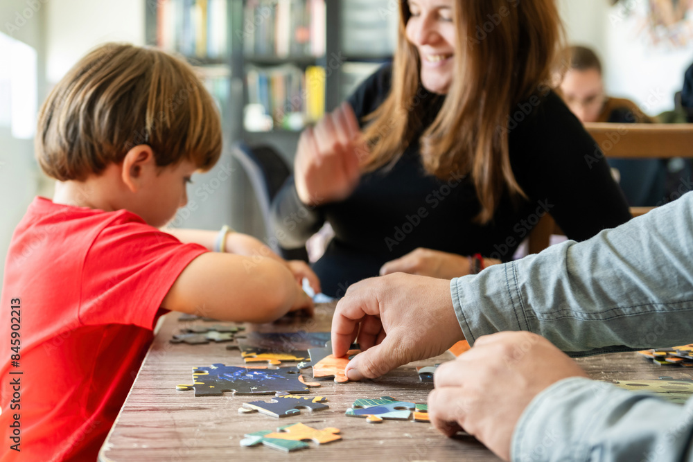 Focused boy assembling jigsaw puzzle with happy crop parents