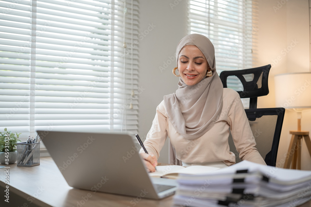 confident Muslim Woman Working at Home Office, Wearing Hijab, Using Laptop and Writing Notes, Modern Workspace with Natural Light, Professional and Productive Atmosphere confident Muslim Woman Working at Home Office, Wearing Hijab, Using Laptop and Writing Notes, Modern Workspace with Natural Light, Professional and Productive Atmosphere