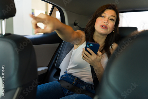 Pretty woman using her smartphone to navigate or request a stop during a ride in a modern car sharing service photo