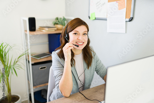 Smiling woman working at a startup, managing tasks with headset in a modern office, portraying friendly customer service and professionalism