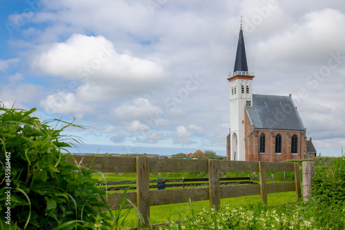 Typical landscape of Texel island with small village and picturesque church (Hervormde kerk) under blue sky and white clouds, A little town on the wadden islands, Den Hoorn, Noord Holland, Netherlands photo