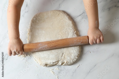 Little child rolling raw dough at white table, top view