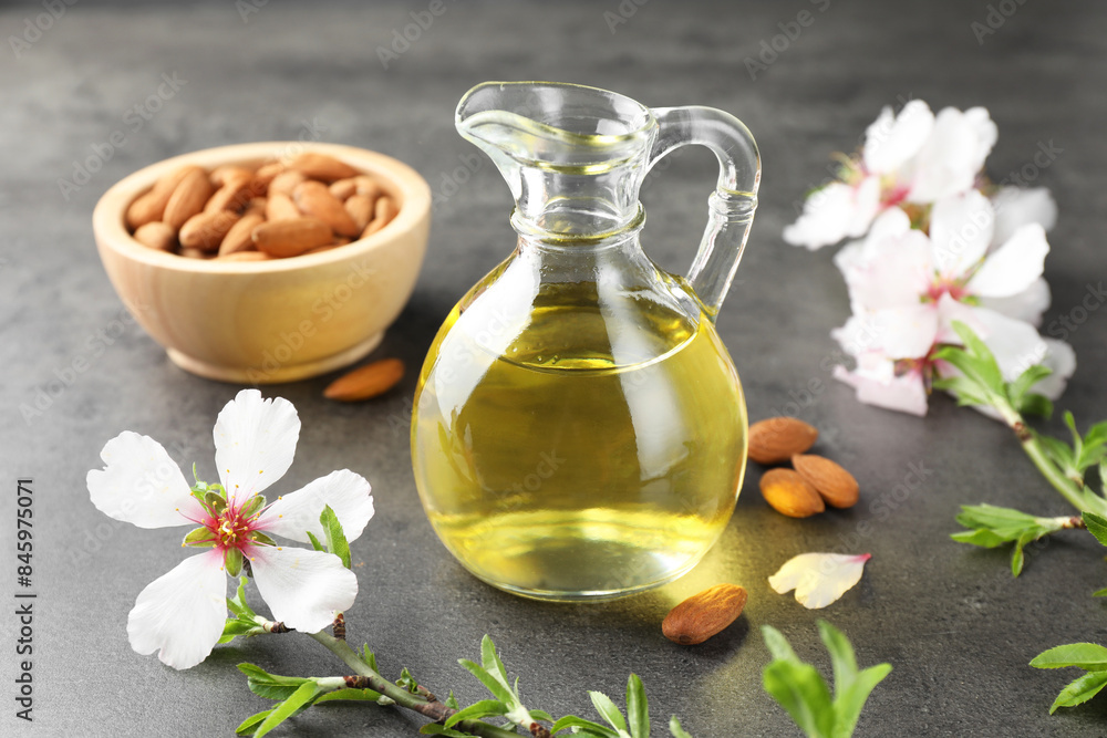 Almond oil in jug, branch with flowers and nuts on grey textured table, closeup Almond oil in jug, branch with flowers and nuts on grey textured table, closeup